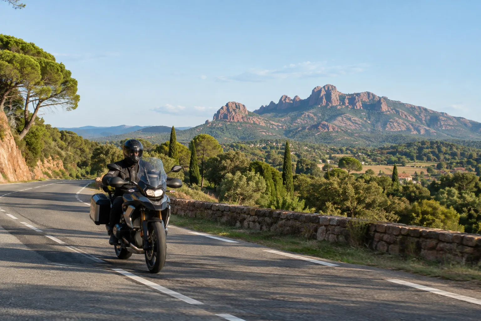 Une moto roule sur une route près de Roquebrune-sur-Argens, avec les collines provençales à l’horizon.