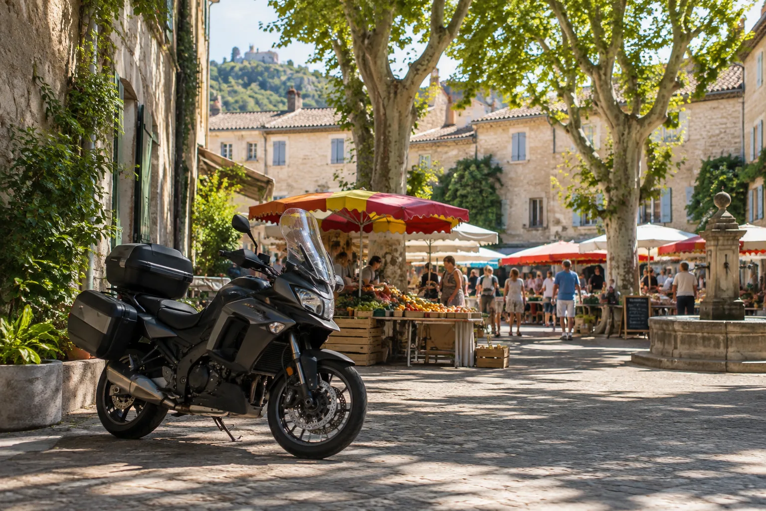 Une moto stationnée près d’une place provençale où des étals de marché se déploient sous les platanes.