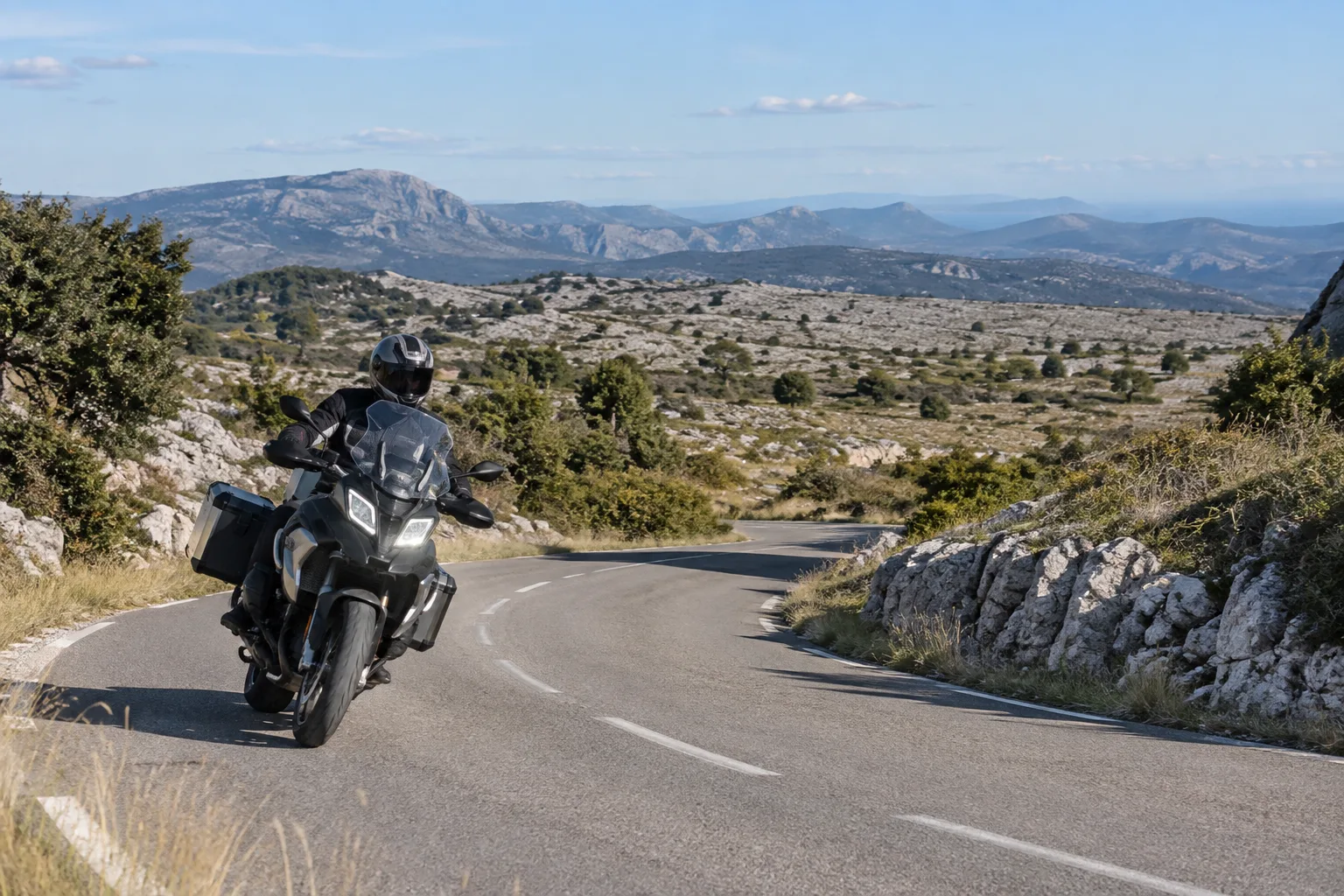 Une moto suit une route sinueuse sur le plateau calcaire de Caussols, entre végétation basse et reliefs ouverts.