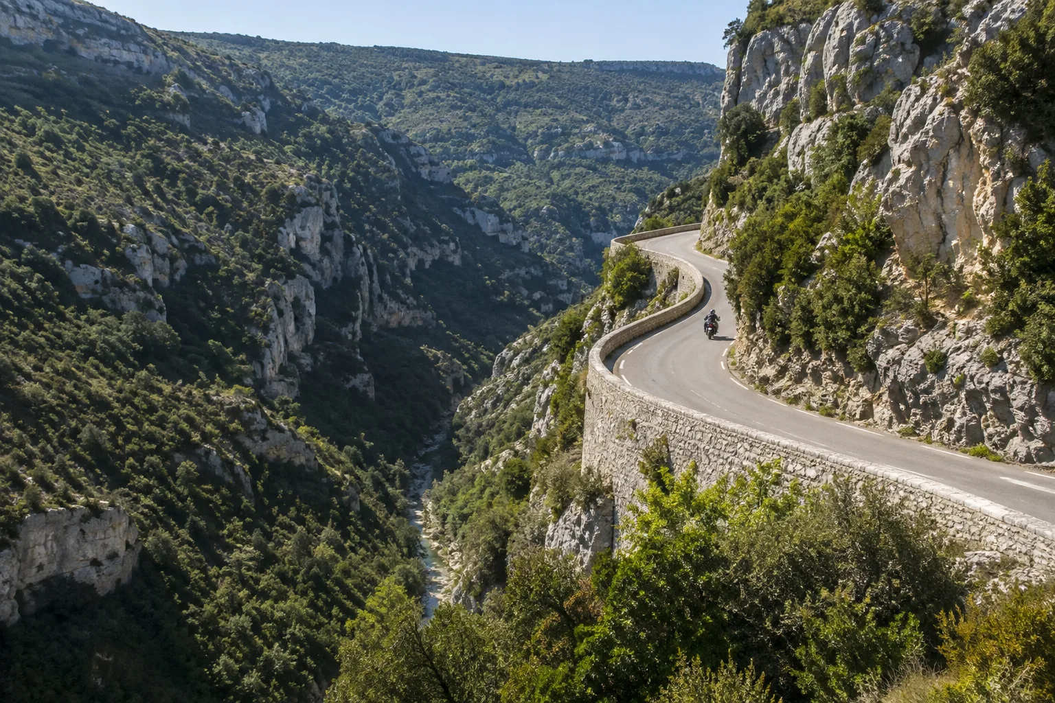 Une moto roule sur une route bordée de falaises calcaires dans les gorges de la Nesque.
