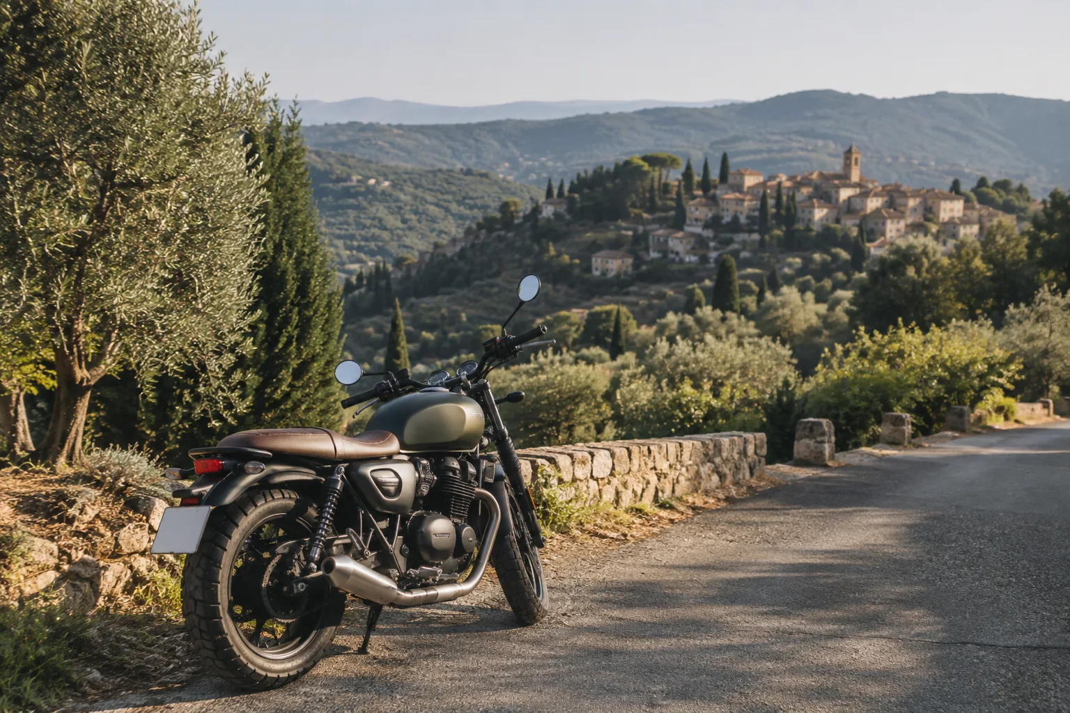Une moto stationnée sur une route de l’arrière-pays, face à des collines boisées et à un village provençal.