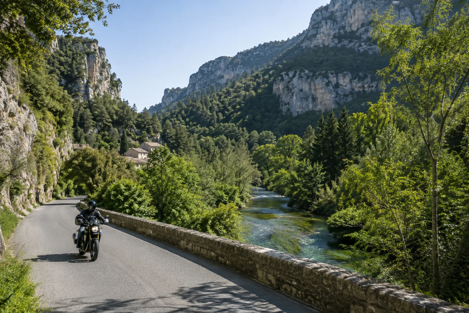 Une moto suit une route de vallée près de Fontaine-de-Vaucluse, entre la Sorgue et des falaises boisées.