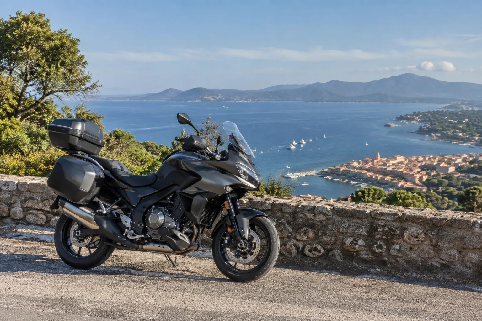 Une moto arrêtée sur une route en surplomb du golfe de Saint-Tropez, avec le littoral et les collines au loin.