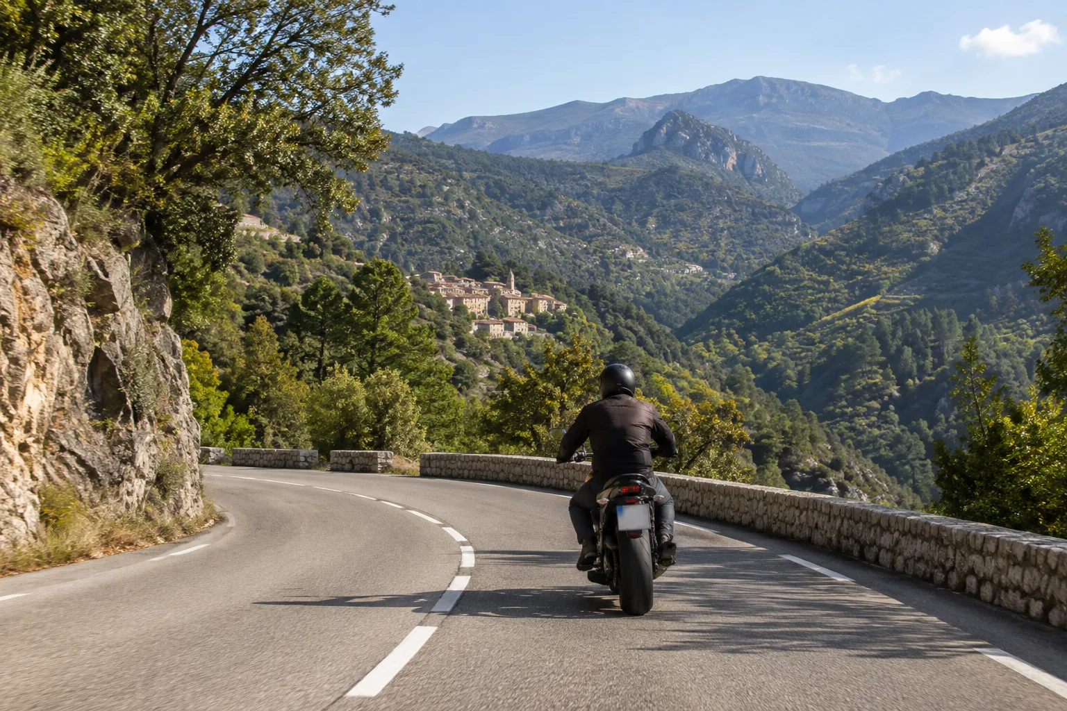 Un motard suit une route sinueuse au milieu des collines boisées de l’arrière-pays niçois.
