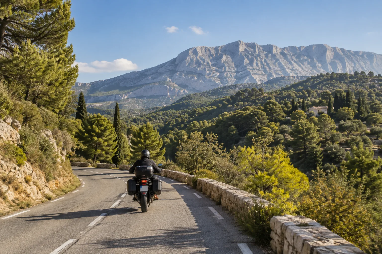 Un motard circule sur une route près de Vauvenargues, avec le relief de Sainte-Victoire en arrière-plan.