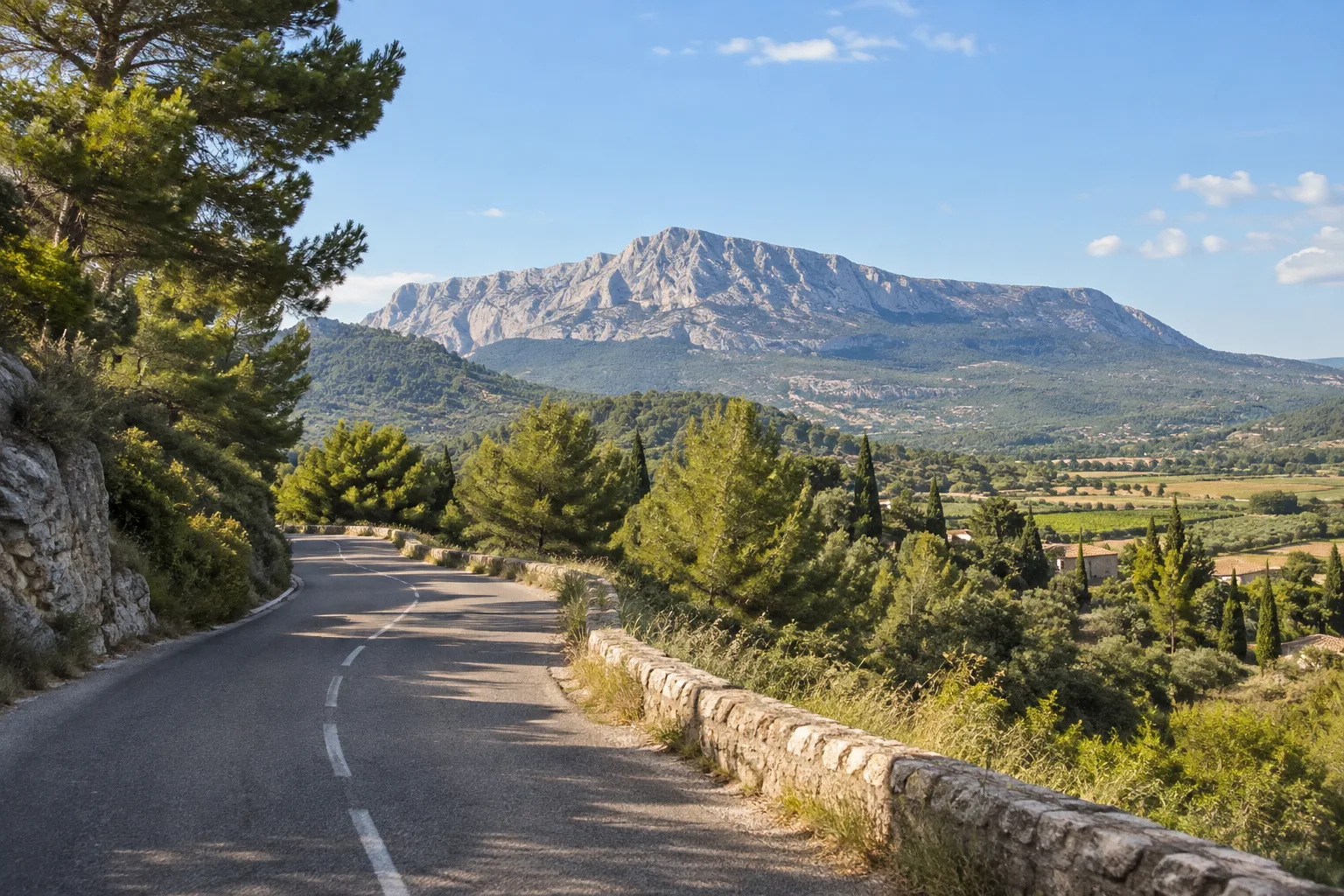 Route de piémont bordée de végétation avec la montagne Sainte-Victoire en arrière-plan.