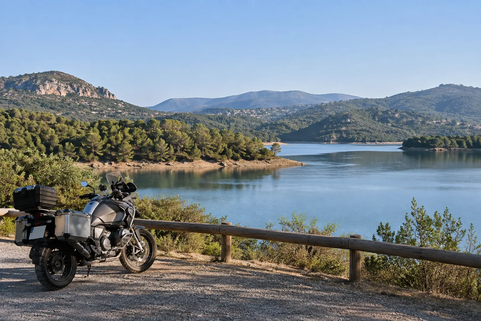 Une moto est stationnée près des rives du lac de Saint-Cassien, face à l’eau et aux collines.
