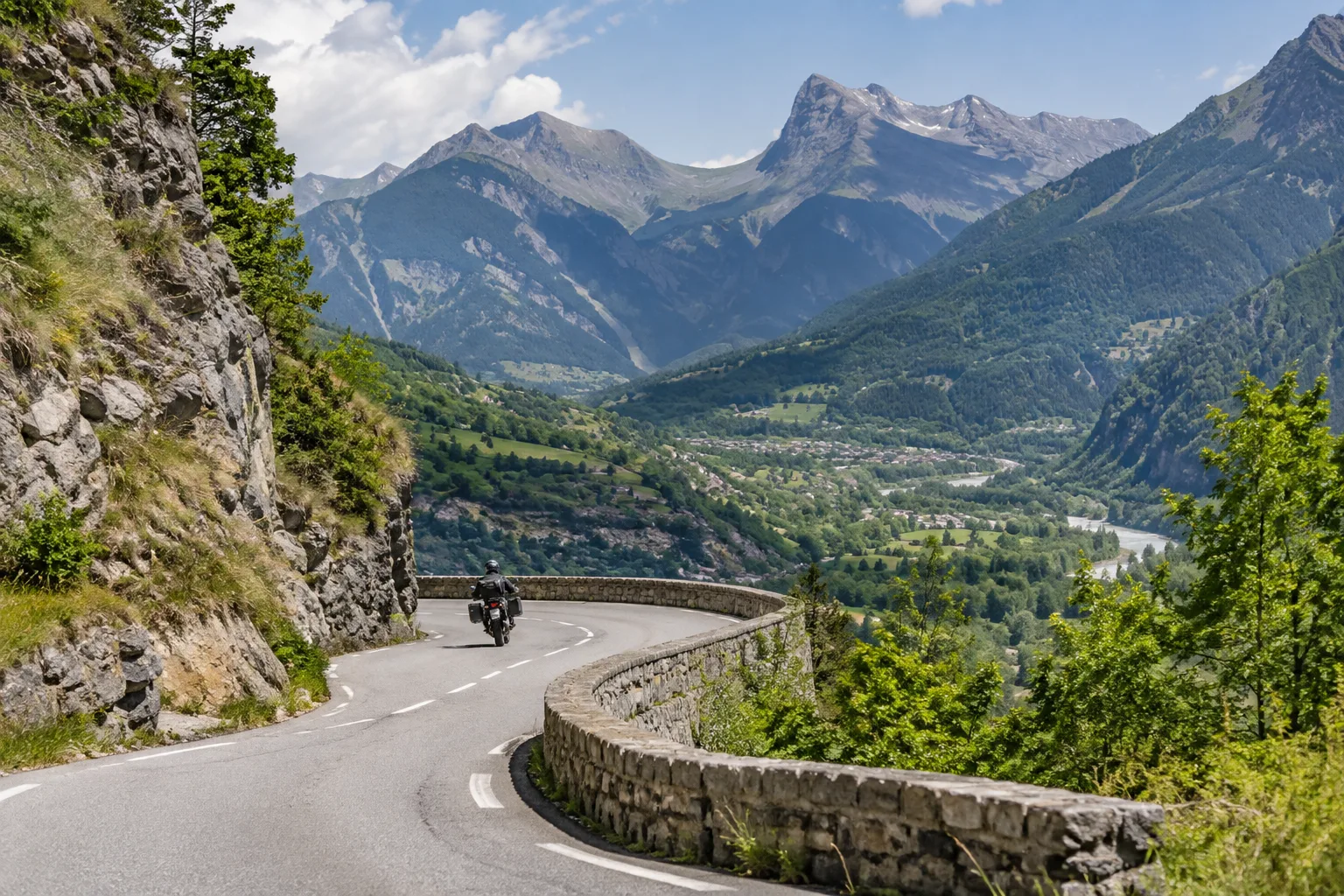 Une moto suit une route sinueuse dans la vallée de l’Ubaye, avec les reliefs alpins en arrière-plan.