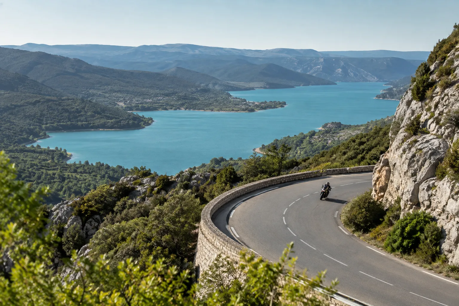 Une moto suit une route de la rive sud du Verdon avec le lac visible au loin.